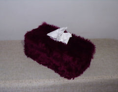 Maroon fuzzy tissue box with a white tissue on a beige surface.