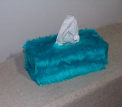 Turquoise fuzzy tissue box with a tissue peeking out on a light surface.